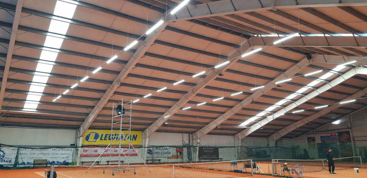 Indoor tennis courts with suspended linear LED lights beneath the roof