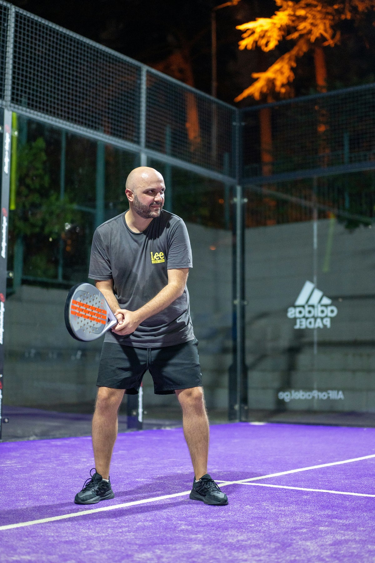 Padel player holding a racket on an illuminated outdoor court at night