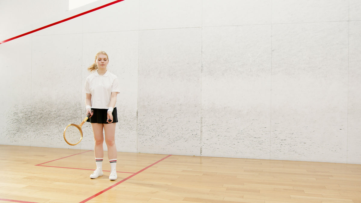 Player on an indoor squash court with white walls and a wooden floor